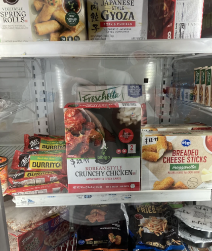 A grocery store freezer section displaying various frozen foods, perfect to buy in bulk—spring rolls, Japanese gyoza, burritos, Korean style crunchy chicken, breaded cheese sticks, and a Freschetta pizza.