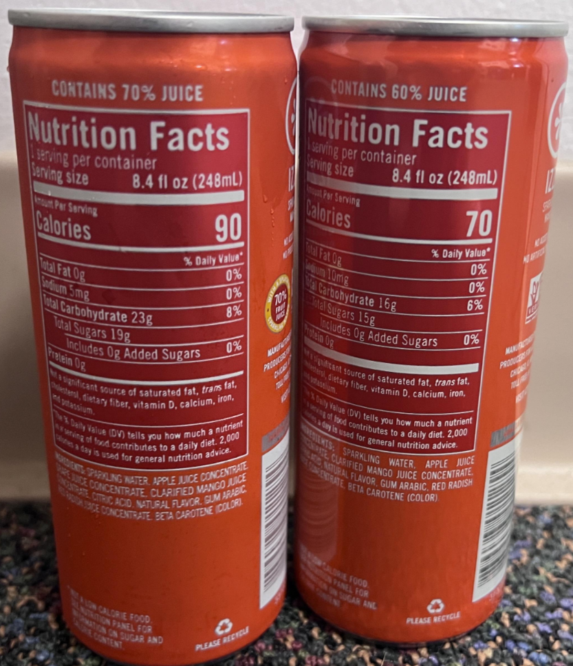 Two orange cans with nutrition facts labels visible. The left can contains 70% juice and 90 calories per 8.4 fl oz serving; the right can contains 60% juice and 70 calories per 8.4 fl oz serving. Both are on a speckled counter.
