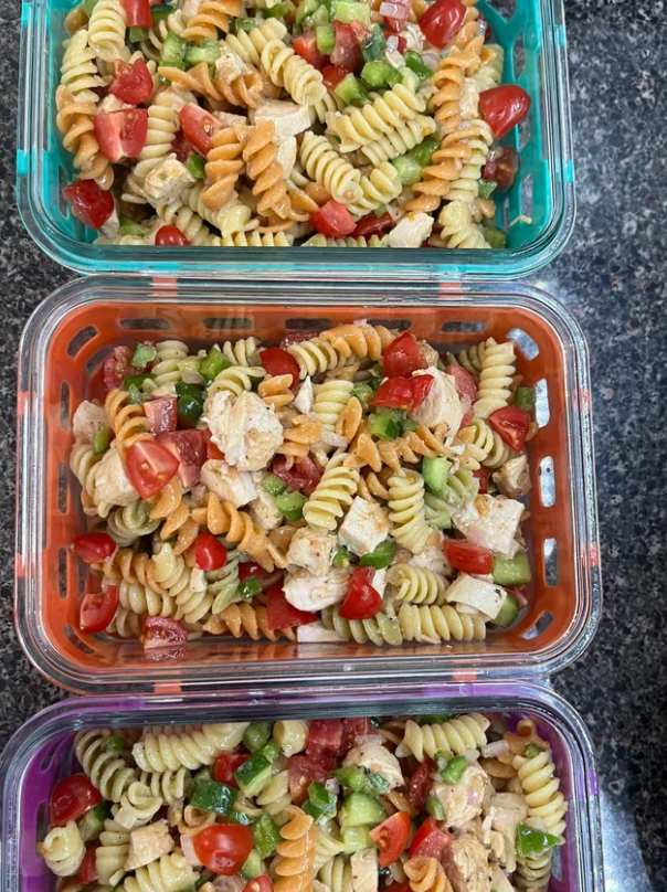 Three containers filled with a colorful pasta salad—rotini, diced chicken, green bell pepper, and cherry tomatoes—sit on a dark granite countertop, showcasing the freshness of cooking from scratch.