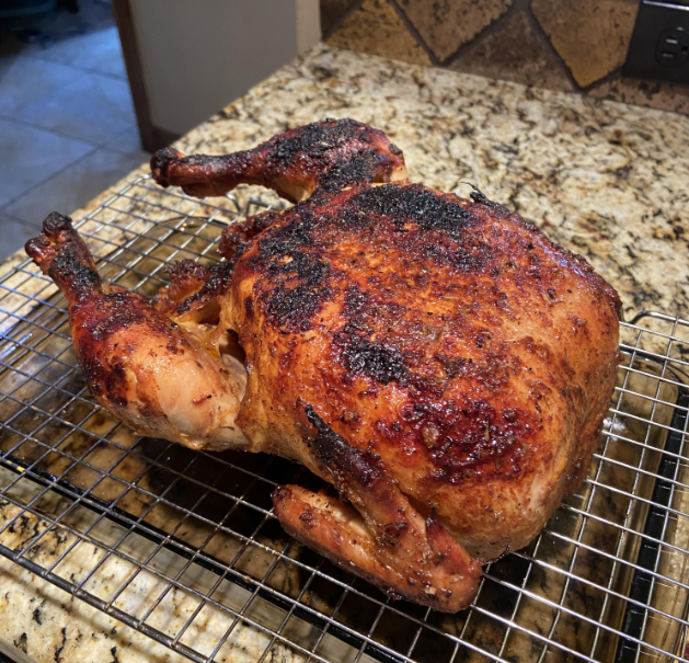 A whole roasted chicken with crispy, golden-brown skin rests on a wire rack over a granite countertop—a delicious example of cooking from scratch, well-seasoned and freshly cooked.