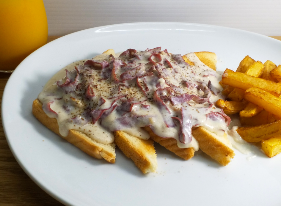 A plate with toast topped with creamy chipped beef gravy, a classic among budget meals, is accompanied by golden French fries. A glass of orange juice is partially visible in the background.