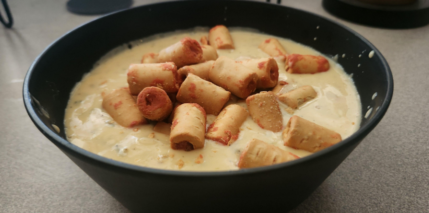 A black bowl filled with creamy yellow soup or sauce, topped with several short, thick, cylindrical breadsticks or snacks arranged unevenly on top—perfect for those seeking delicious and satisfying budget meals.