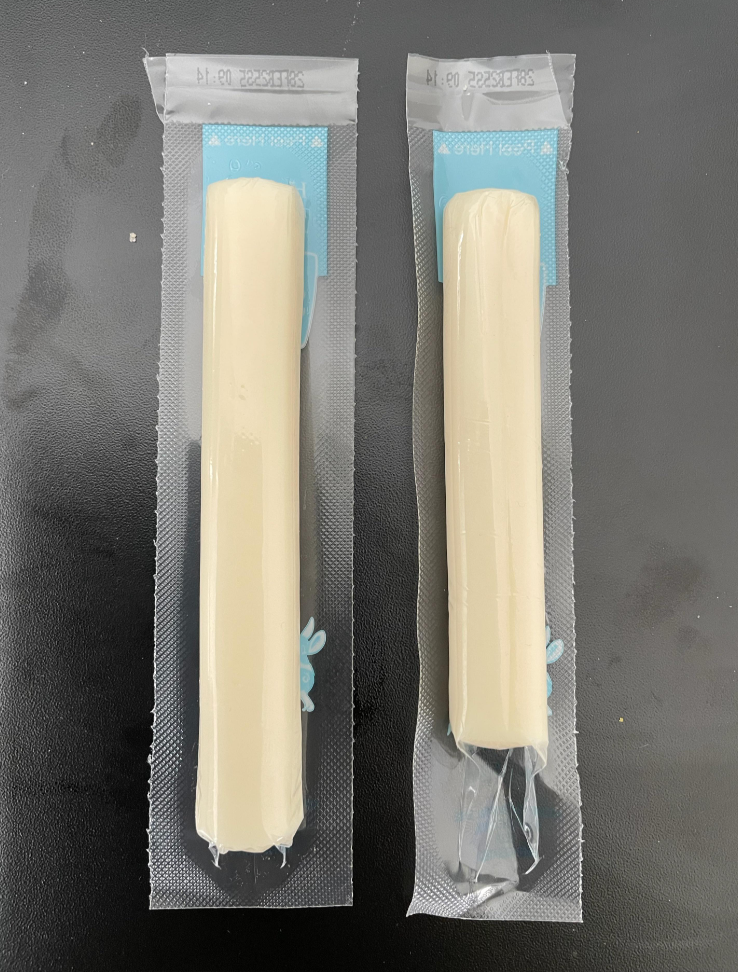 Two individually wrapped sticks of string cheese are placed side by side on a dark surface.