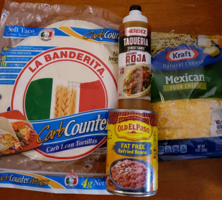 A package of La Banderita Carb Counter tortillas, a can of Old El Paso fat free refried beans, Herdez taqueria street sauce, and Kraft Mexican shredded cheese—all essentials for tasty budget meals—rest on a wooden surface.