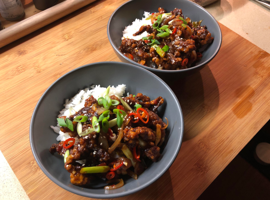 Two grey bowls filled with white rice topped with stir-fried vegetables, crispy meat, chopped green onions, and red chili slices—perfect budget meals for quick and delicious dining, all placed on a wooden surface.