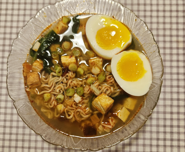 A bowl of ramen with noodles, tofu, greens, and a soft-boiled egg cut in half—perfect for those seeking delicious budget meals.