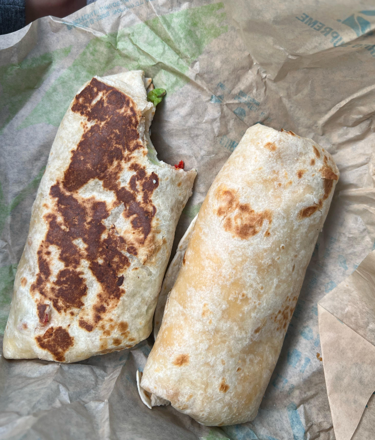 Two burritos on brown paper, one with a grilled, browned side and a bite taken out, the other whole and untoasted. Both are wrapped in flour tortillas—perfect examples of satisfying fast-food value meals.