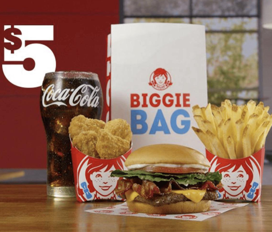 A Wendy's Biggie Bag meal—cheeseburger, fries, chicken nuggets, and a Coca-Cola drink—is displayed on a table, highlighting one of the best fast-food value meals. A large "$5" sign appears on the left.