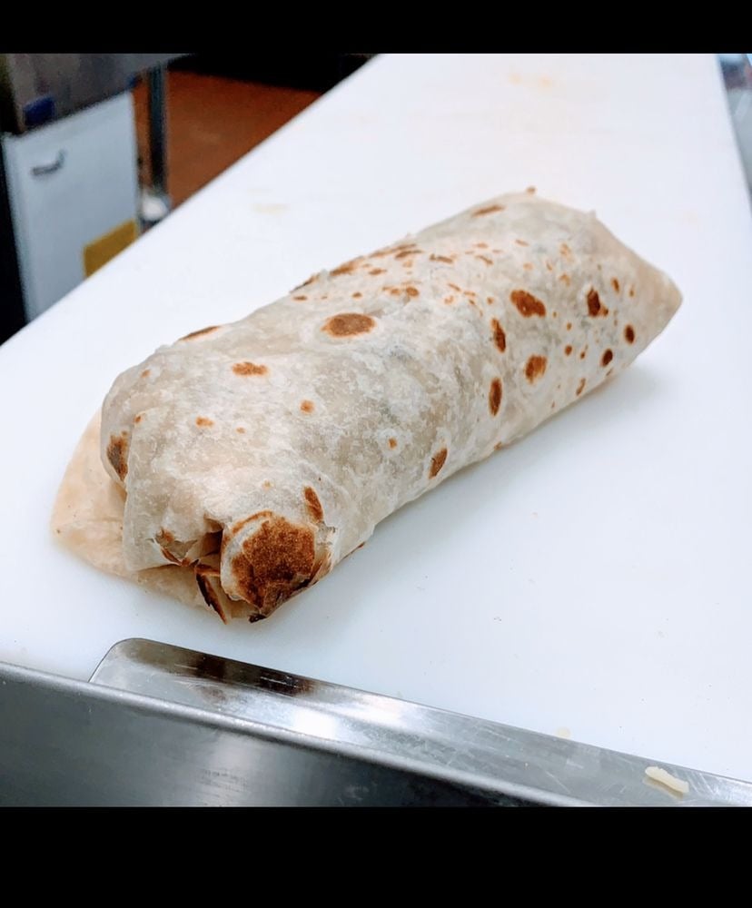 A large, wrapped burrito with a lightly toasted flour tortilla sits on a white cutting board in a kitchen setting, reminiscent of the delicious offerings from top breakfast burrito spots.