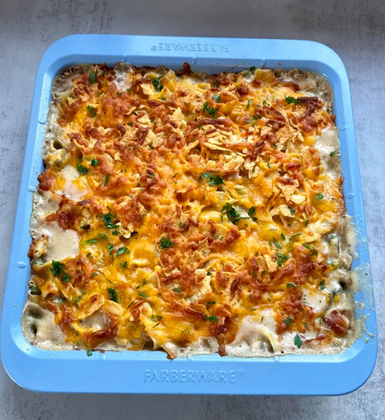 A classic casserole—like the comforting meals middle-class moms cooked—topped with melted cheese, crispy fried onions, and chopped herbs sits in a blue square baking dish on a light-colored surface.