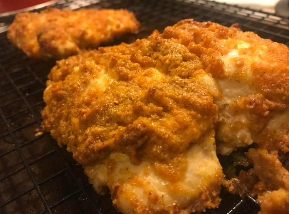 Close-up of crispy, golden-brown fried chicken pieces resting on a black wire cooling rack—a classic comfort food reminiscent of the hearty meals middle-class moms cooked. The textured breading appears crunchy and well-cooked.