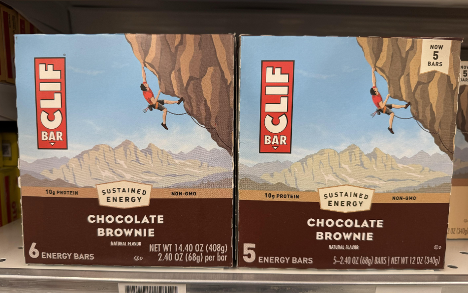 Two boxes of Clif Bar Chocolate Brownie energy bars on a store shelf, each featuring an illustration of a climber scaling a cliff with mountains in the background.