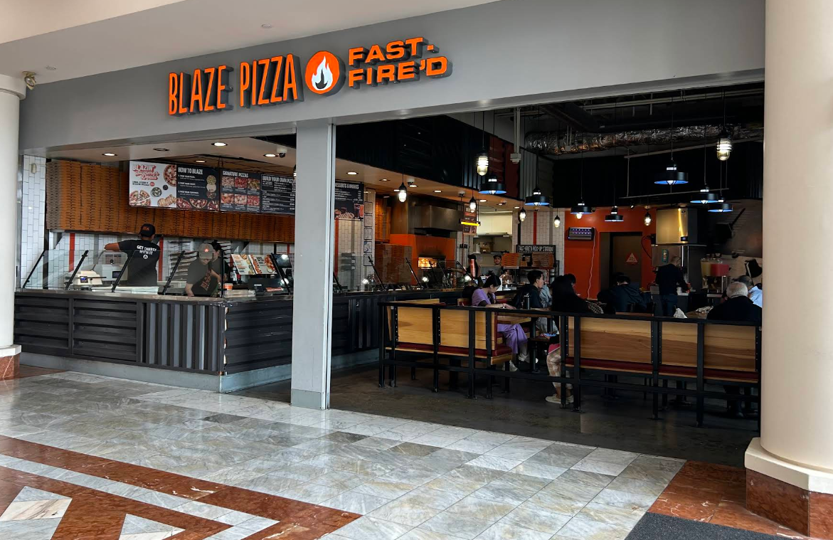 Blaze Pizza, one of the popular pizza chains, is located in a mall with an orange sign above the entrance. Staff work behind the counter while customers dine at tables inside, surrounded by black and orange decor and visible menu boards.