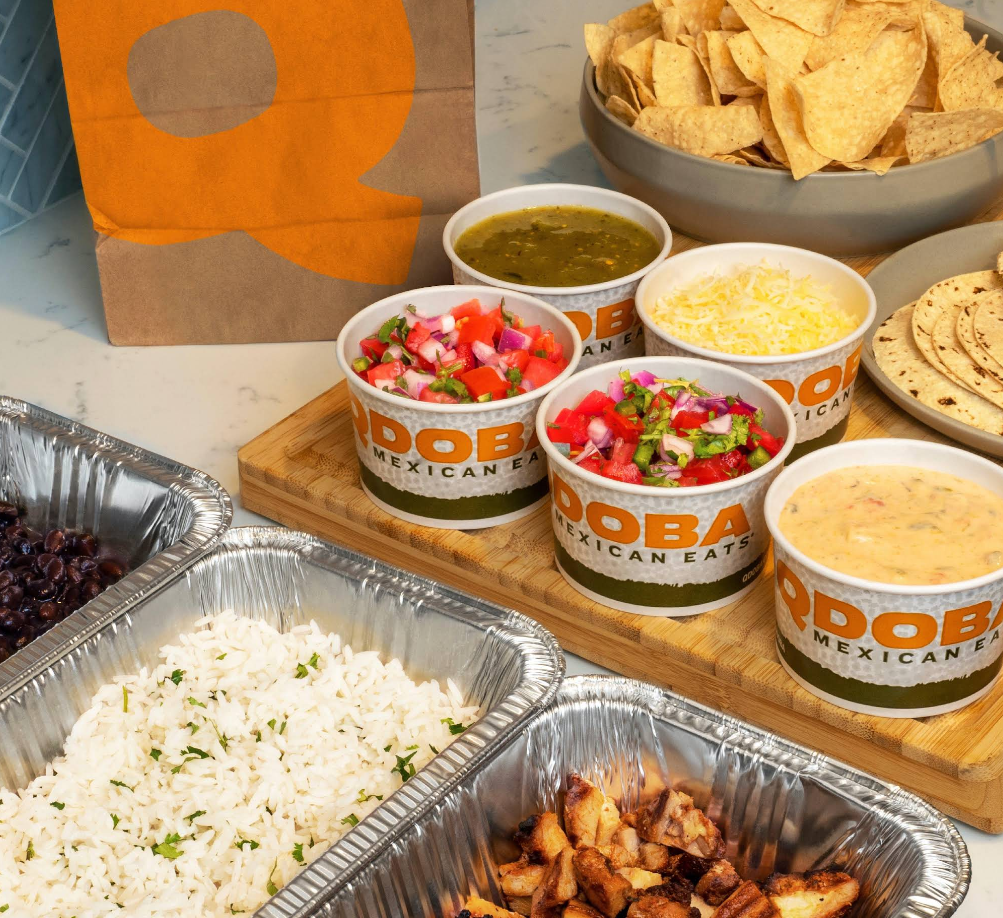 An assortment of QDOBA Mexican Eats catering dishes—rice, black beans, seasoned chicken, pico de gallo, shredded cheese, green salsa, queso, flour tortillas, and tortilla chips—showcases the flavors of one of the top Mexican food chains.