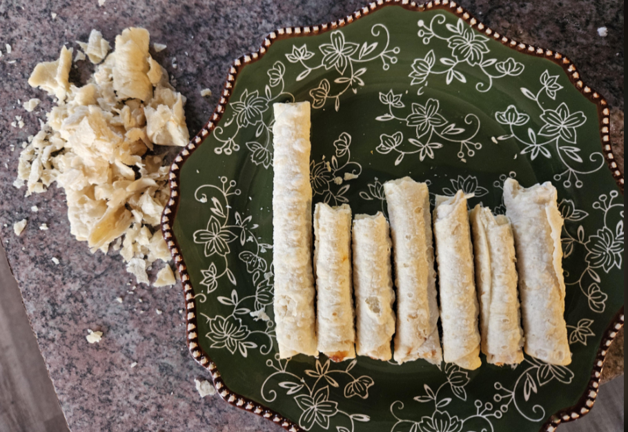 Eight pieces of cassava on a decorative green plate with a floral pattern, with some crumbled cassava off to the side on a granite countertop.