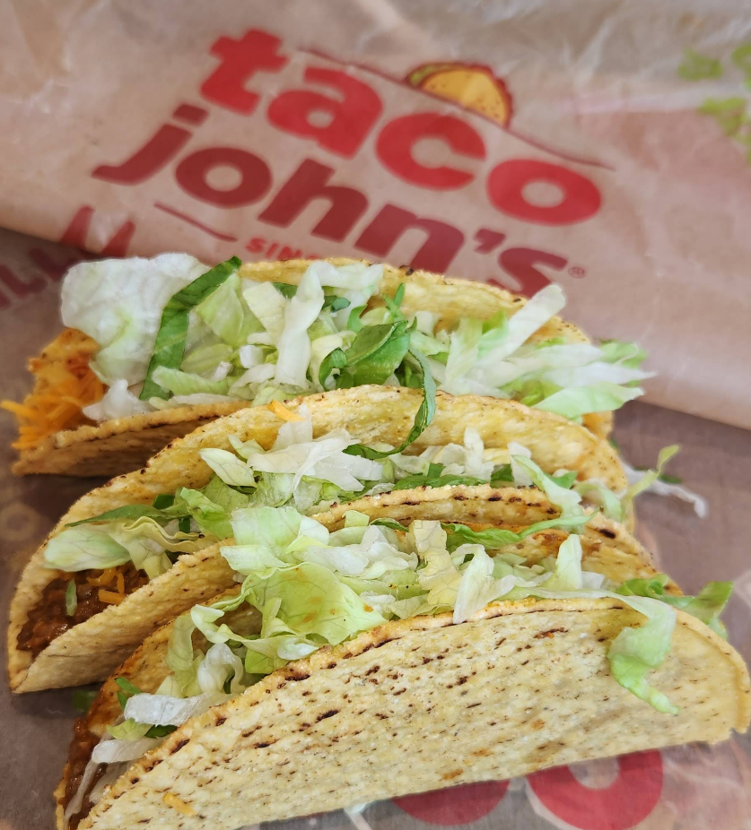 Three hard shell tacos filled with seasoned meat, shredded lettuce, and cheese, served on a Taco John’s branded wrapper—a delicious choice among Mexican food chains.
