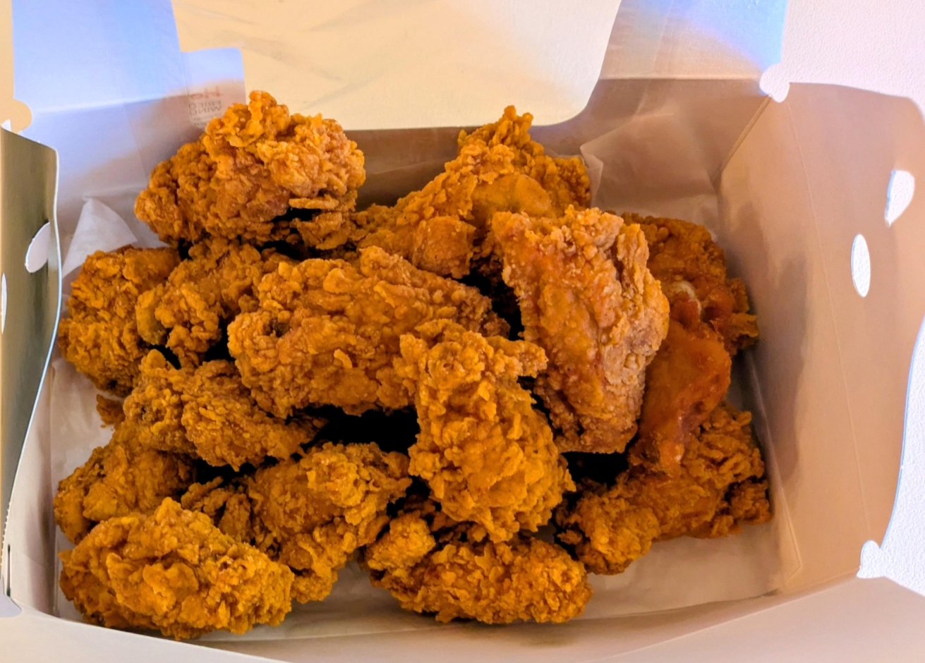 A box filled with several pieces of crispy, golden-brown fried chicken—just like those from popular fried chicken chains—placed on white paper inside a white takeout container.