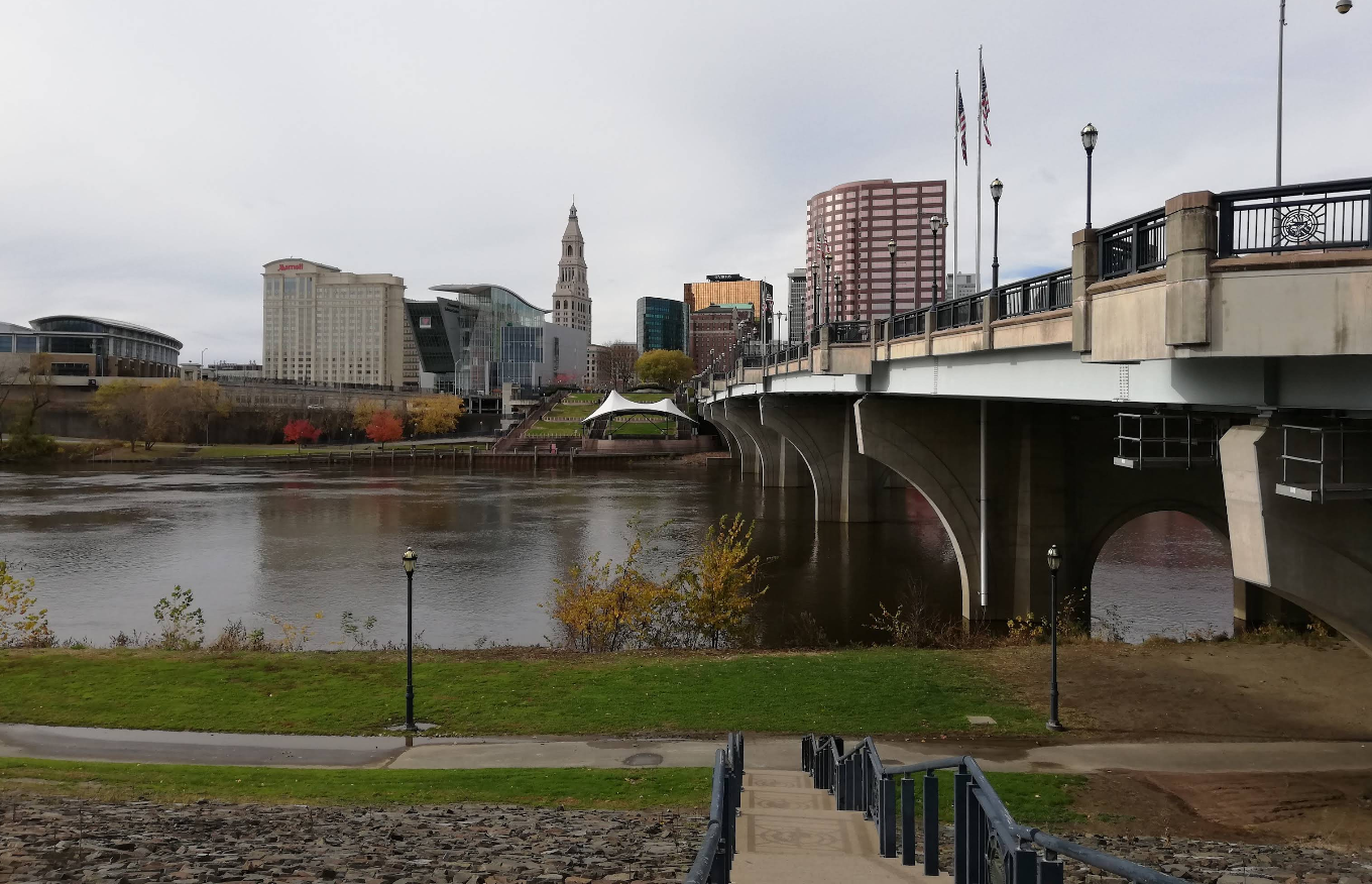 A city skyline with modern and historic buildings stands beside a concrete bridge over a wide river, with a park and green grass in the foreground—an inviting scene far removed from the stresses of credit card debt.
