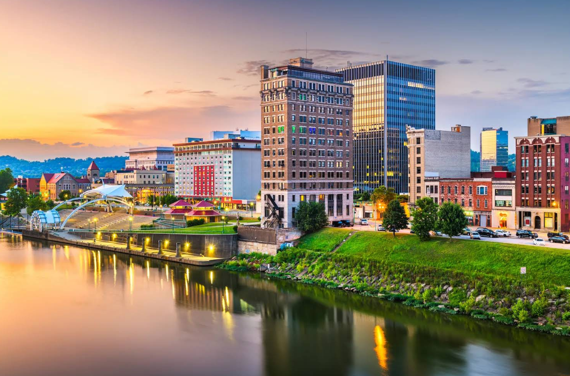Downtown cityscape at sunset with tall buildings, a riverside walkway, and reflections on the calm water, featuring greenery along the riverbank and a colorful sky—an oasis of calm far from daily worries like credit card debt.