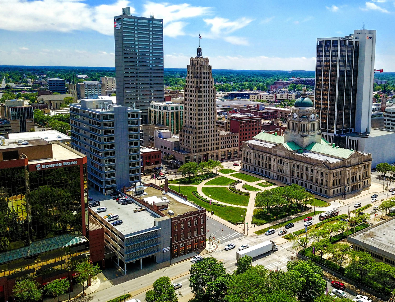 Aerial view of a cityscape featuring a historic courthouse with a domed roof, surrounded by tall modern buildings, green lawns, and busy streets where the challenges of credit card debt are part of daily urban life under a partly cloudy sky.