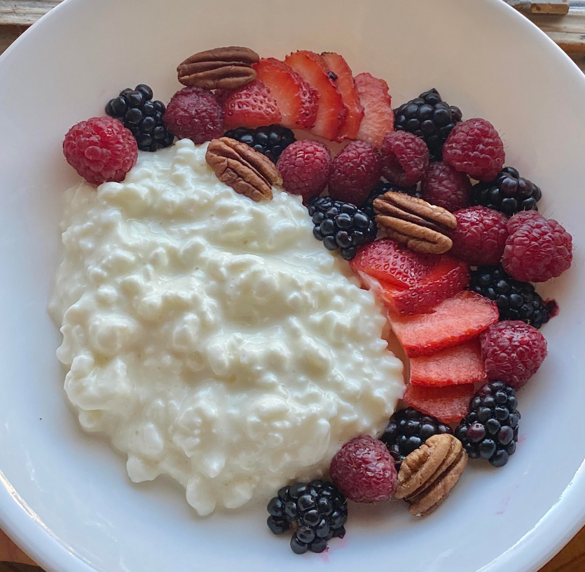 A white bowl filled with cottage cheese—a classic among foods that boomers still eat—topped with fresh raspberries, blackberries, sliced strawberries, and a few pecan halves, all neatly arranged on one side.