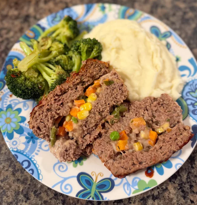 A plate with two slices of meatloaf stuffed with mixed vegetables, a serving of mashed potatoes, and steamed broccoli—all classic foods that boomers still eat—served on a floral-patterned dish.