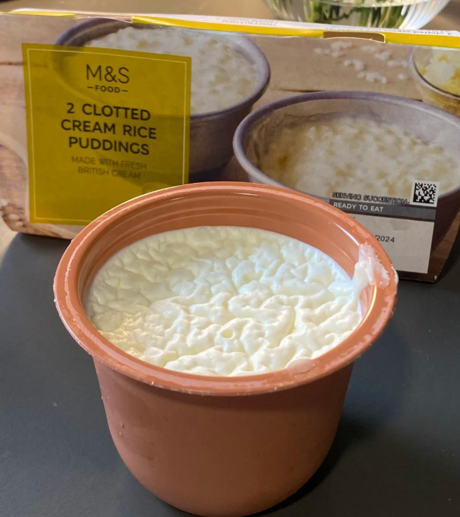 A small brown pot filled with clotted cream rice pudding sits in front of its packaging, capturing the nostalgic appeal of foods that boomers still eat, with images of rice puddings and the label “M&S 2 Clotted Cream Rice Puddings.”