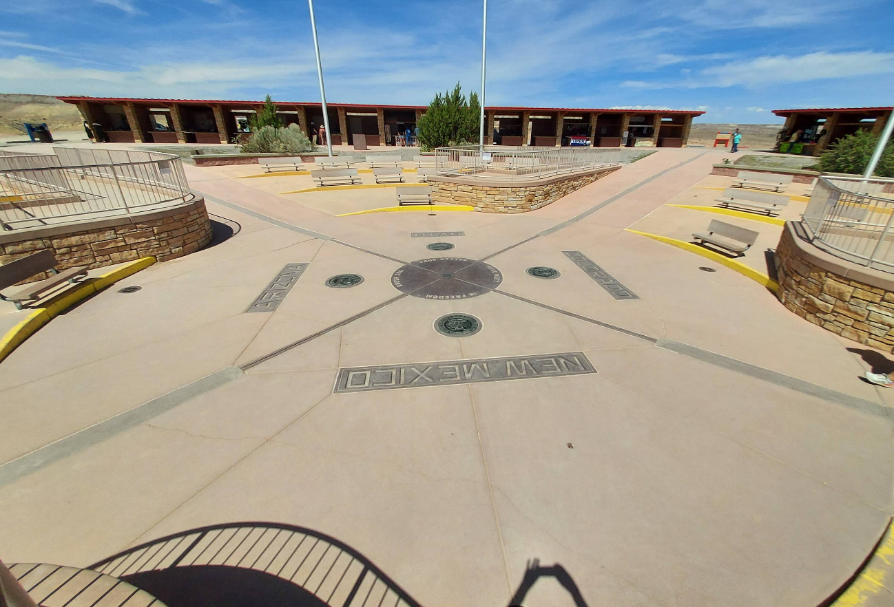 A concrete plaza marks the Four Corners Monument, one of the unique tourist attractions where Arizona, Colorado, New Mexico, and Utah meet; plaques for each state border surround a central medallion, with benches and visitors in the background.