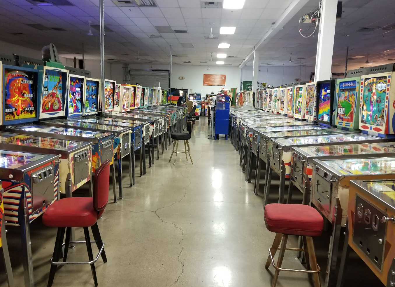 Rows of vintage pinball machines line both sides of a wide aisle in this brightly lit arcade, one of the unique Las Vegas attractions, with polished concrete floors and empty stools scattered along the vibrant machines.