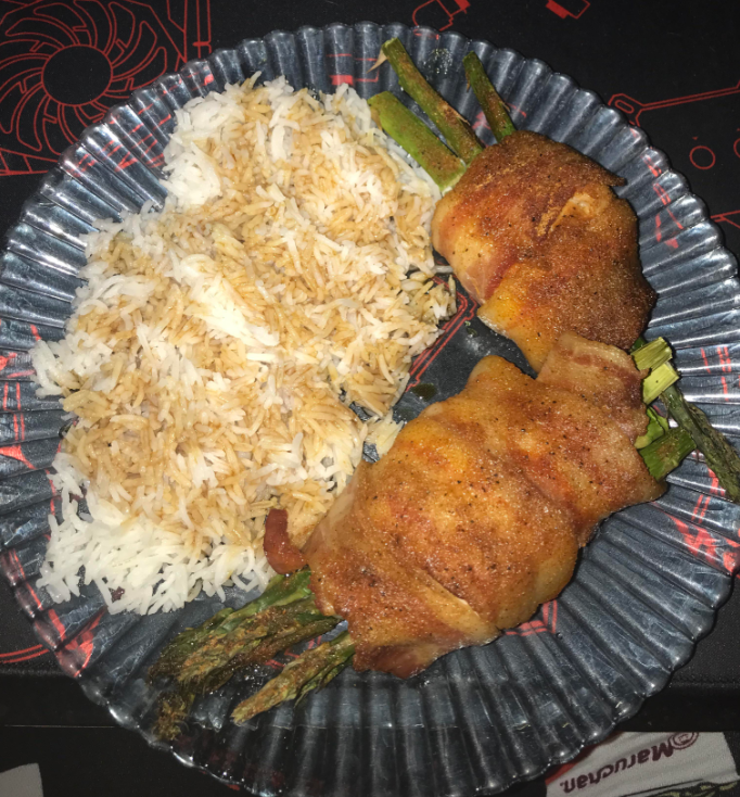A glass plate with white rice mixed with brown sauce, and two bundles of asparagus wrapped in bacon and seasoned, placed side by side—perfect to stretch food for a satisfying and flavorful meal.