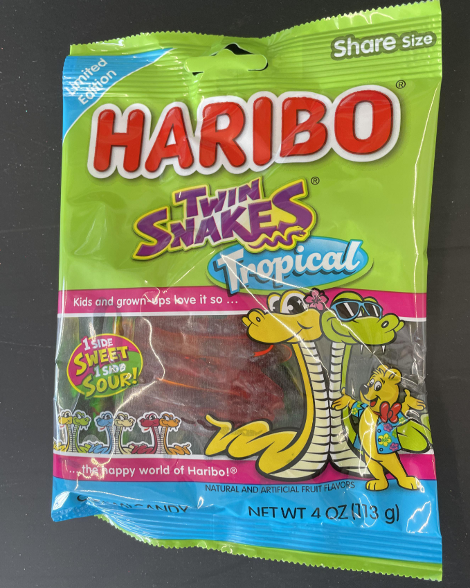 A green and blue bag of Haribo Twin Snakes Tropical, the best gummy candy, features cartoon snake characters and bold colorful text. The package notes "Limited Edition" and "Share Size," with 4 oz (113 g) of candy inside.