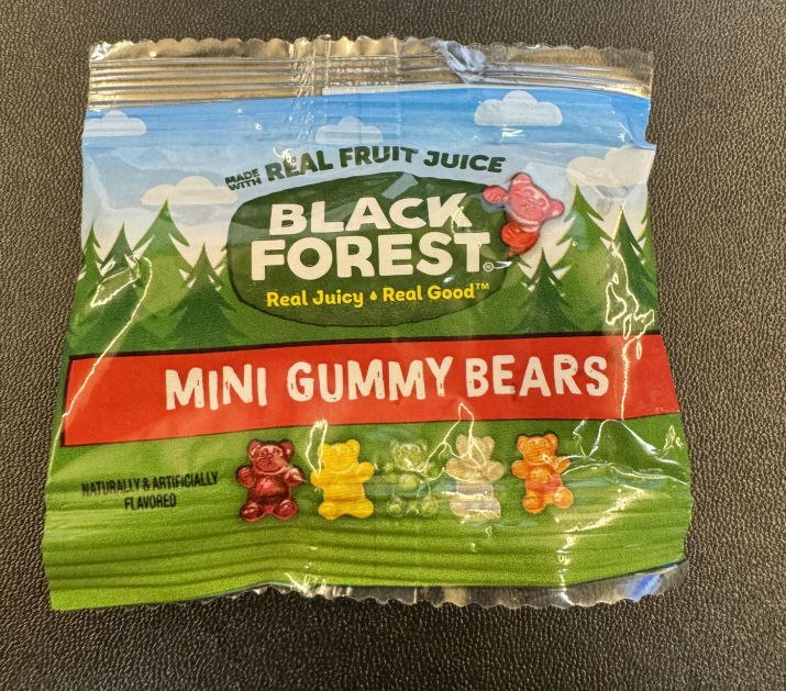 A small, sealed package of Black Forest Mini Gummy Bears, featuring cartoon gummy bears and forest imagery on a green and blue background. The label highlights "Real Fruit Juice," making it one of the best gummy candy options around.