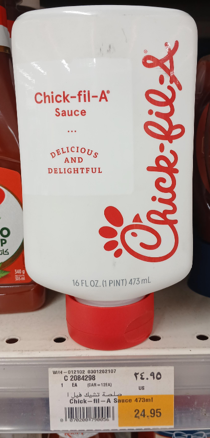 A 16 fl. oz. (473 ml) bottle of Chick-fil-A Sauce, a favorite among fast-food sauces, with red text and logo is displayed on a store shelf for 24.95. Other condiments are partially visible around it.