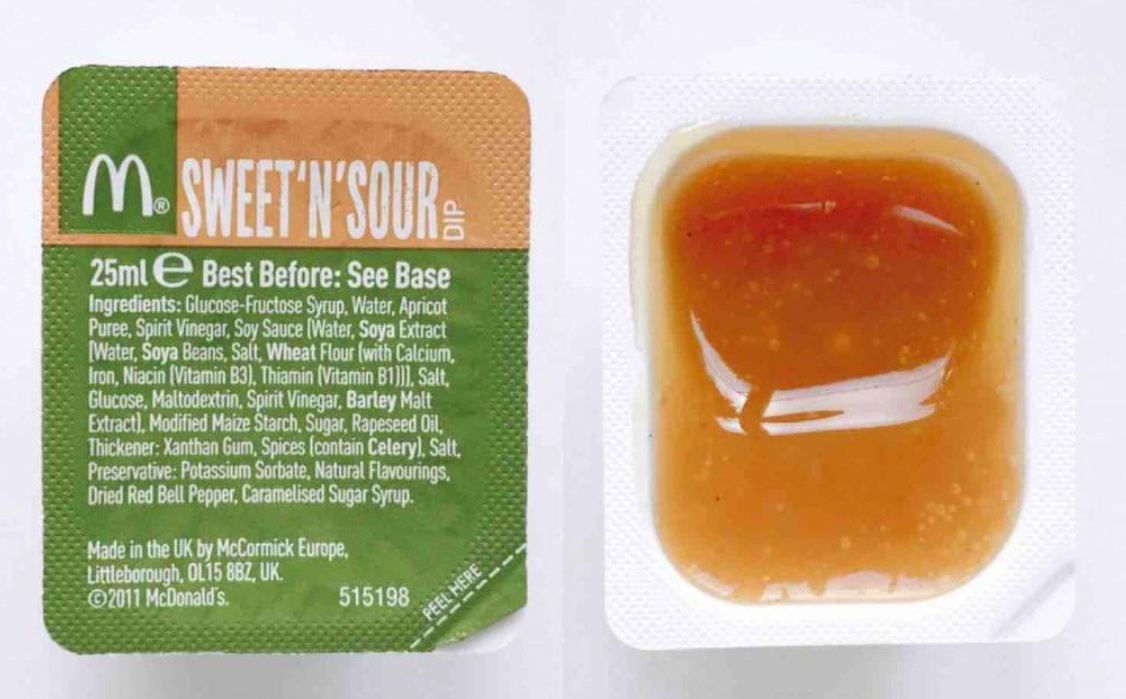A McDonald's Sweet 'N' Sour dip packet, part of their popular fast-food sauces lineup, is shown opened. The green labeled lid on the left lists ingredients and expiration details, while the orange sauce is visible in the tray on the right.