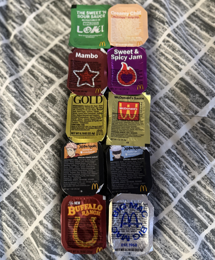 Nine fast-food sauces, each with different flavors and colorful labels, are arranged in a 3 by 3 grid on a gray and white patterned fabric background.