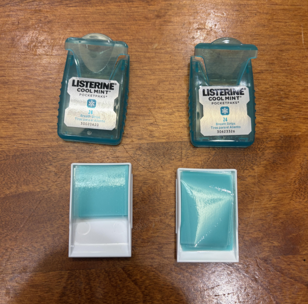 Two open and two closed Listerine Cool Mint PocketPaks containers are arranged on a wood surface, showing the teal breath strips inside both open containers.