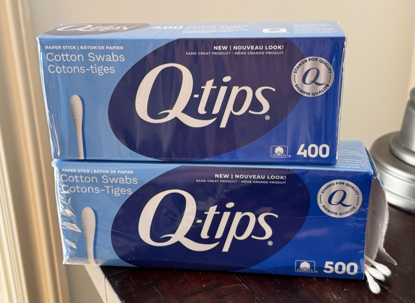 Two blue boxes of Q-tips cotton swabs are stacked on a table. The top box contains 400 swabs and the bottom box contains 500 swabs. Both boxes display the brand name prominently.