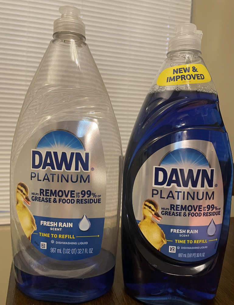 Two bottles of Dawn Platinum dishwashing liquid, both labeled "Fresh Rain" scent, stand side by side on a table. The bottle on the right has a "New & Improved" yellow label at the top.