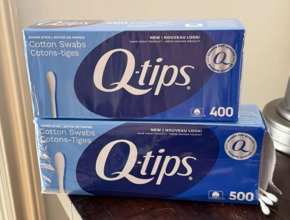 Two boxes of Q-tips cotton swabs are stacked, one containing 400 swabs and the other 500. Both boxes are blue and display the Q-tips logo with "New! Nouveau Look!" text on the packaging.