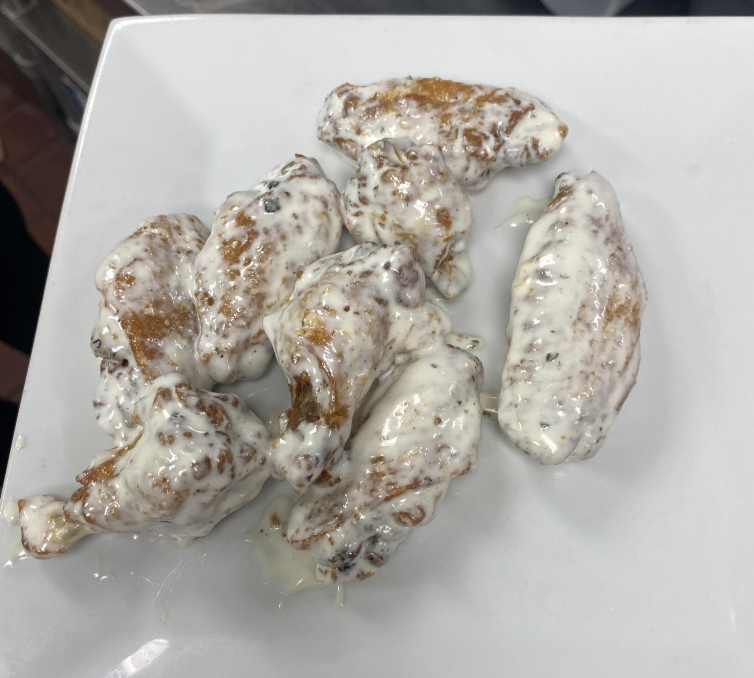 Several chicken wings coated in a creamy white wing sauce are arranged on a square white plate.