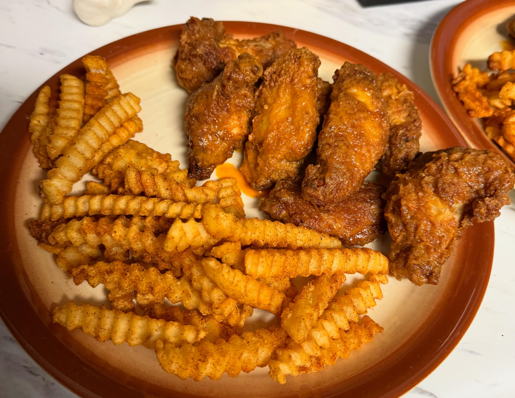 A plate of seasoned crinkle-cut French fries and crispy fried chicken wings with a reddish-brown coating and tangy wing sauces, served on a beige and brown-rimmed ceramic plate.