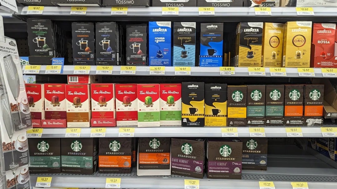 Shelves stocked with various coffee brands, including Lavazza, Tim Hortons, and Starbucks, in K-cup and ground coffee formats—just some of the Walmart products on display. Each row features blends and flavors with visible price tags below each item.