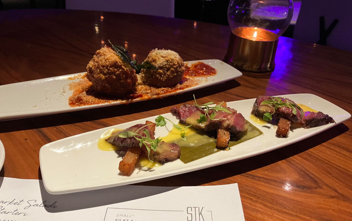 Two rectangular plates with gourmet dishes—one featuring two large, breaded and sauced meatballs, the other sliced steak on sauce with microgreens—reflect how products getting more expensive because of tariffs can elevate even a simple meal out.