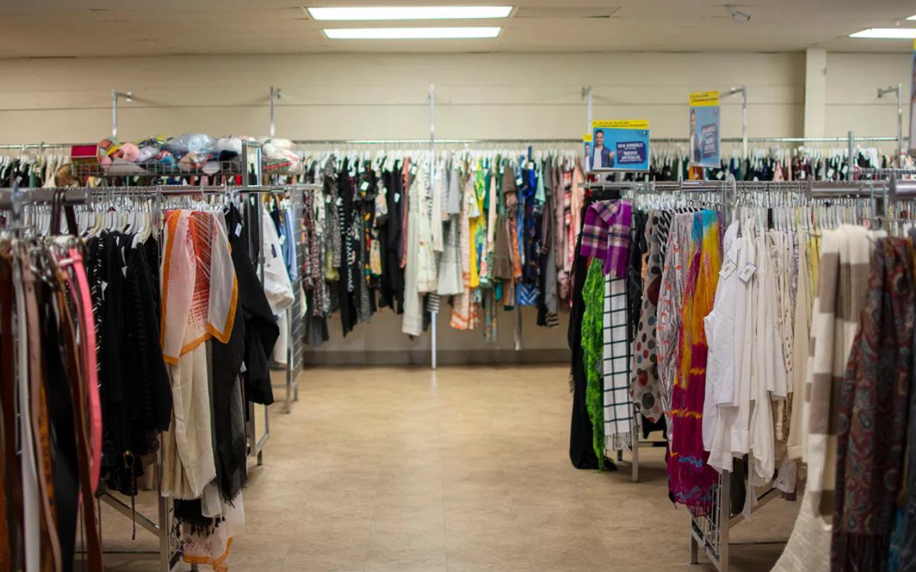 Clothing racks filled with various colorful garments are arranged in rows inside a well-lit store with a tiled floor and cream-colored walls, where products are getting more expensive because of tariffs.