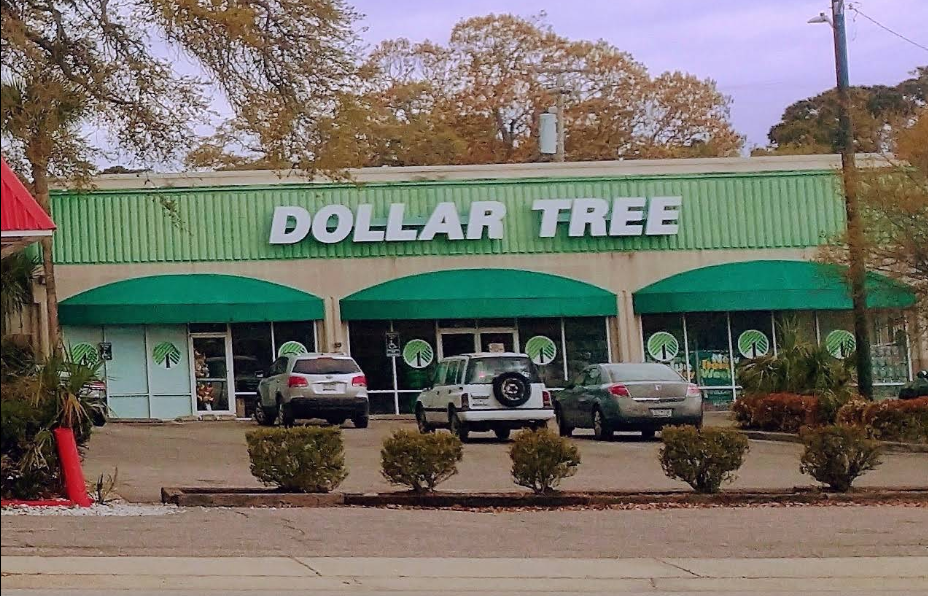 A Dollar Tree store with its signature green awning and large Dollar Tree sign, three vehicles parked out front, and trees with autumn leaves in the background.