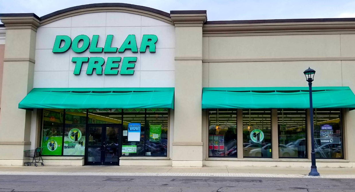 The front of a Dollar Tree store features green awnings, large windows, and a shopping cart outside. The bright green Dollar Tree sign is clearly visible above the entrance.