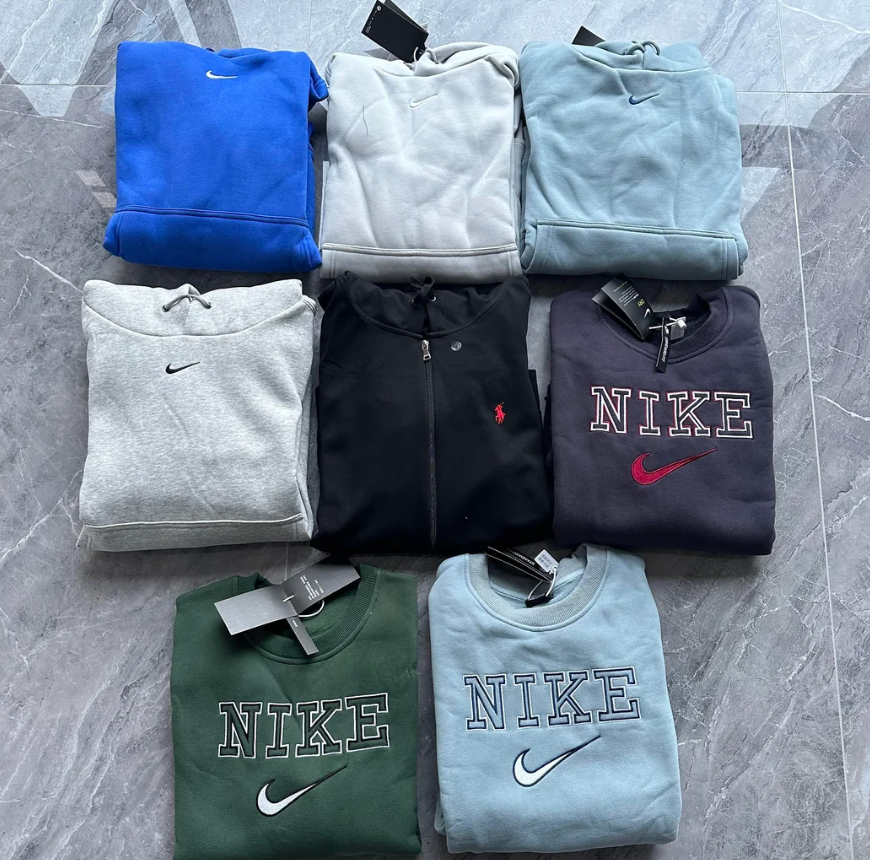 Eight folded sweatshirts on a gray marble floor, including Nike and one black Ralph Lauren hoodie. These clothes come in blue, light gray, dark gray, green, black, and light blue, many with visible tags attached.