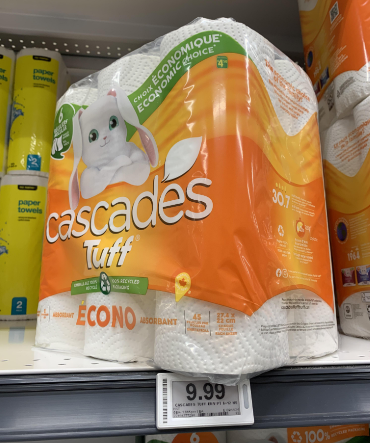 A pack of Cascades Tuff Econo absorbent paper towels with a white bunny on the packaging sits on a supermarket shelf among other grocery items, priced at $9.99. Other paper towel products are visible beside it.