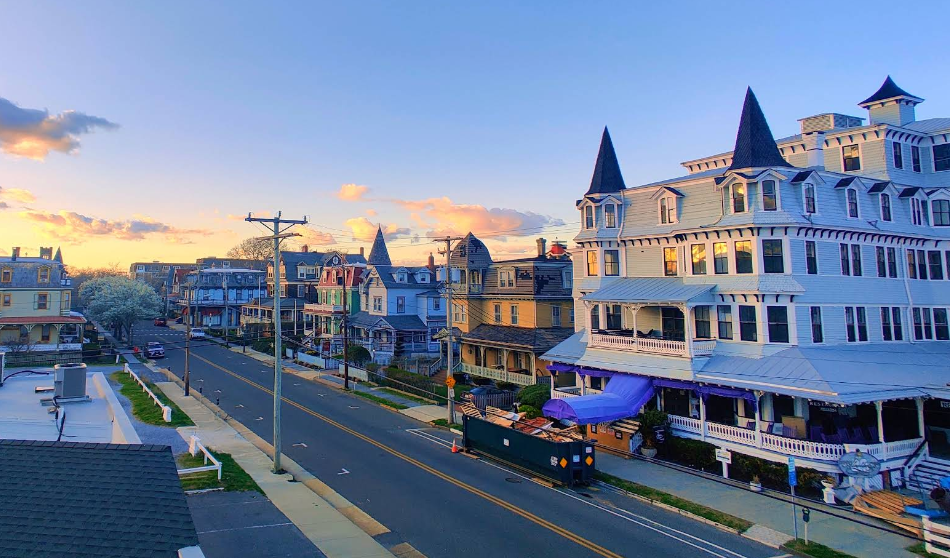 A quiet street lined with Victorian-style houses at sunset evokes the charm of classic beach destinations, featuring ornate architecture, pointed towers, and colorful facades under a clear sky with a few clouds.