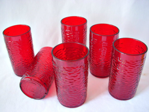 Six textured red glass tumblers are arranged on a white surface, with five standing upright and one lying on its side.